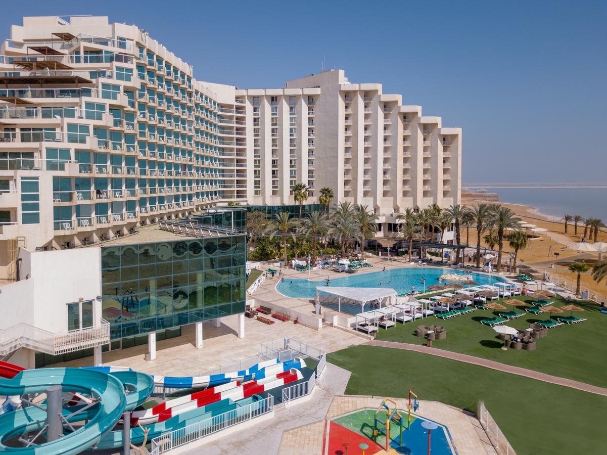 Leonardo Club Hotel Dead Sea Neve Zohar Exterior foto The image shows a large hotel complex alongside a pool area. The hotel features modern architecture with multiple levels and numerous balconies. In front of the hotel, there is a recreational area with a swimming pool, water slides, and lounging chai